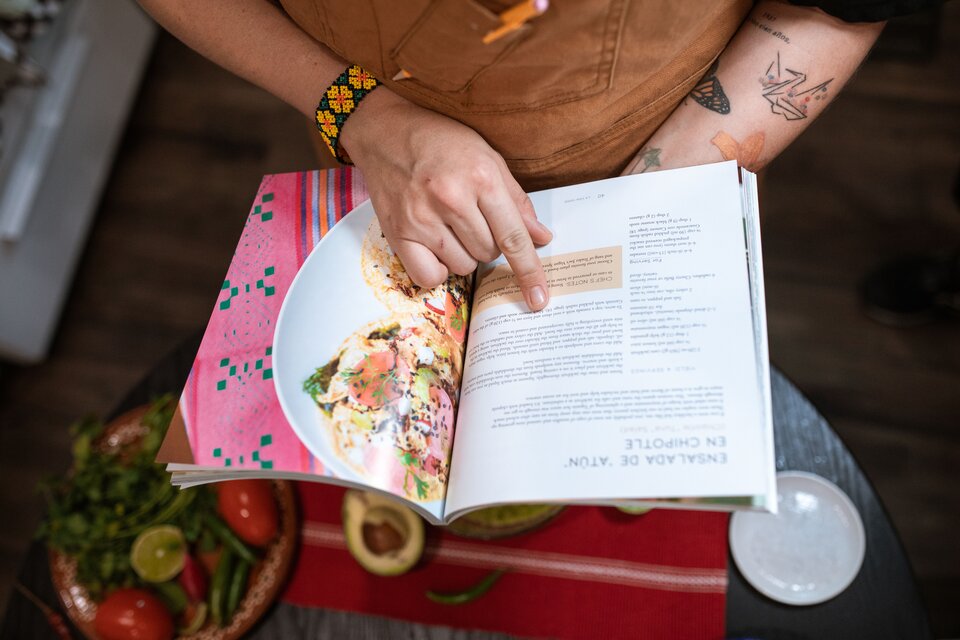 Aufgeschlagenes Kochbuch mit Rezept, in der Hand gehalten am Küchentisch